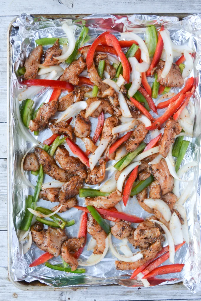 cooked sheet pan chicken fajitas sitting on the aluminum foil-covered pan.