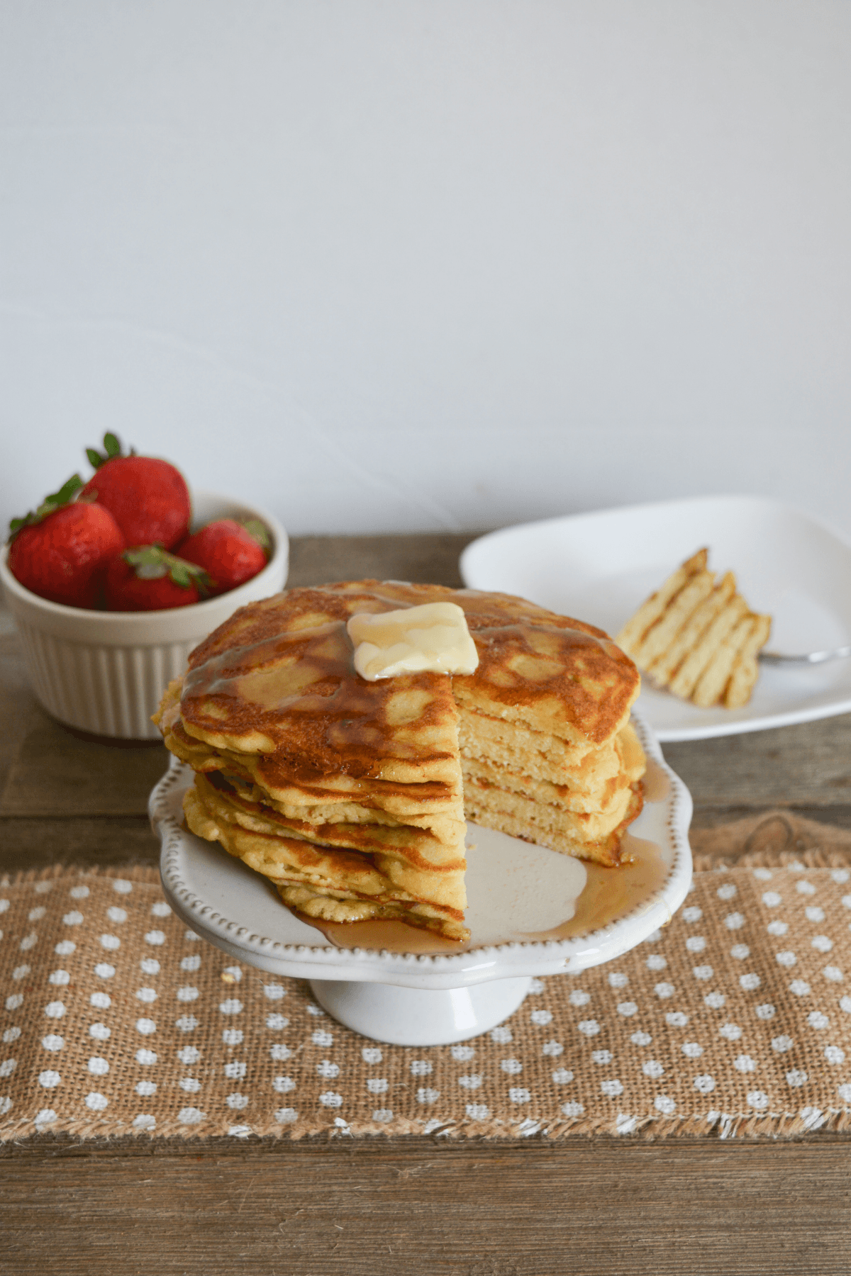 stack of coconut flour keto pancakes, covered with sugar free syrup and a pat of butter, with a slice of the stack taken out and placed in the background